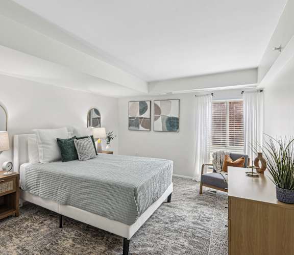 A bedroom with a bed, nightstand, and a plant.