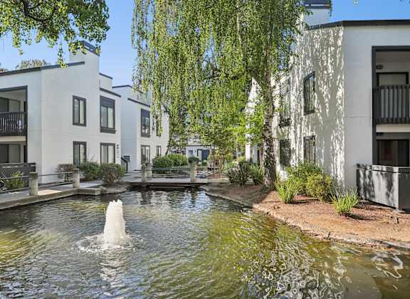 A fountain in the middle of a pond in front of apartment buildings.