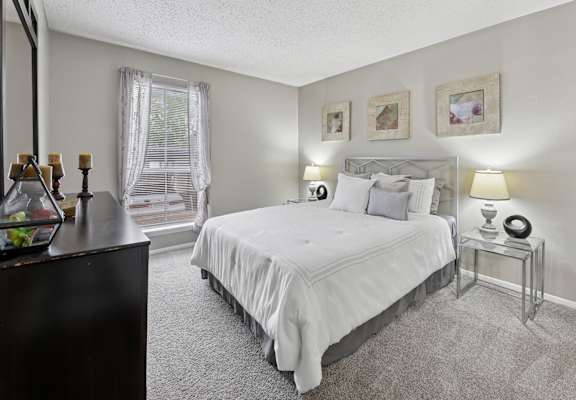 A bedroom with a large bed, a nightstand with a lamp, and a dresser with a mirror.