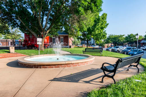 a park with a fountain and benches in front of a red building