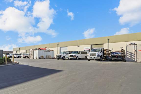 A white car is parked in front of a large warehouse.