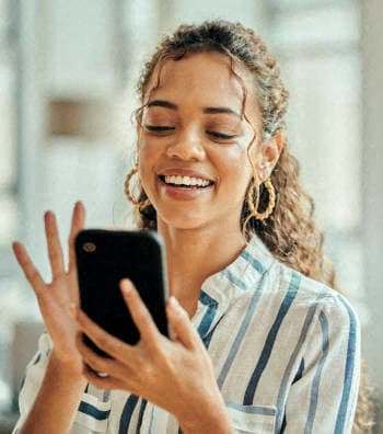 a young woman smiling while looking at her cell phone