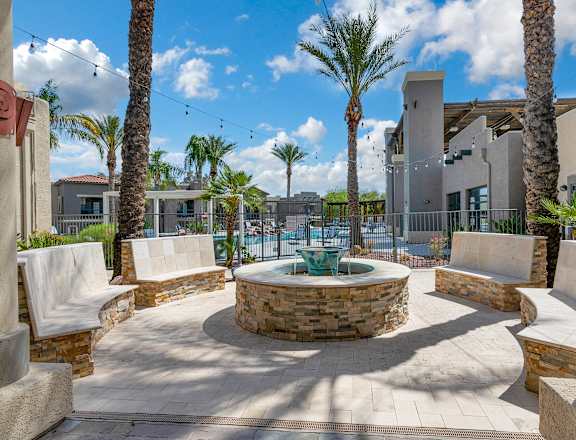 A courtyard with a fountain surrounded by palm trees and concrete pillars.