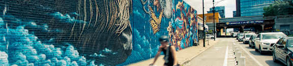 A cyclist rides past a large mural on a city street.