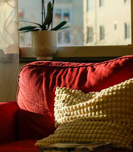 A red couch with a yellow pillow and a book on it.