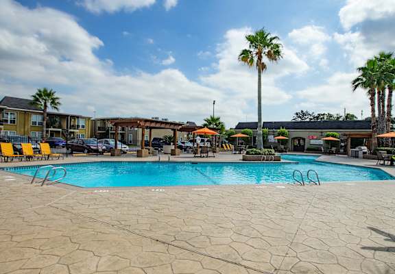 A large outdoor swimming pool surrounded by palm trees and lounge chairs at Willow Creek Apartments, Houston