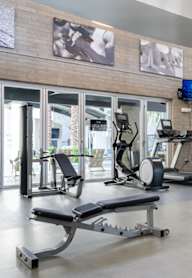 A gym with a variety of equipment including a weight bench, a treadmill, and a television.