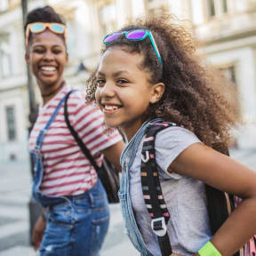 two young girls walking down the street wearing backpacks and smiling
