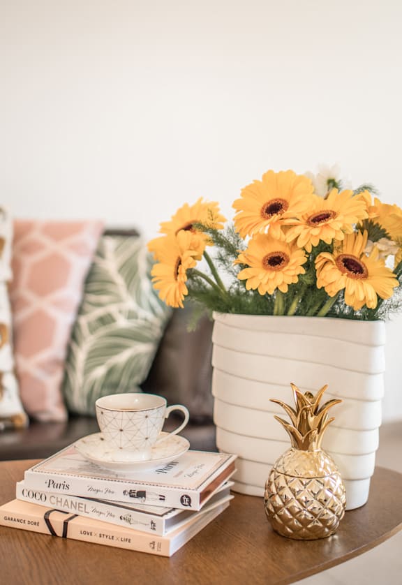 A table with a stack of books, a cup of tea, a pineapple, and a vase of flowers at Bridge City, Oregon