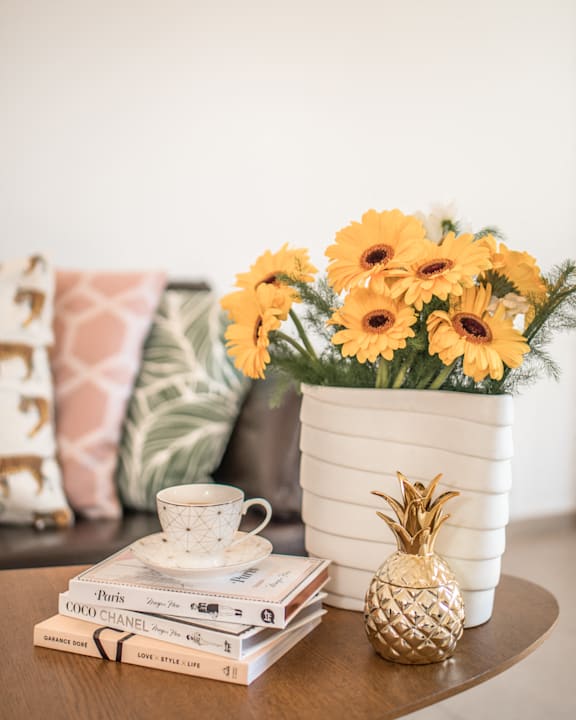 A table with a stack of books, a cup of tea, a pineapple, and a vase of flowers at Coast Pine