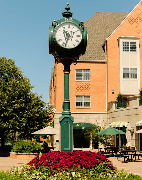 A green clock with roman numerals stands in front of a building.