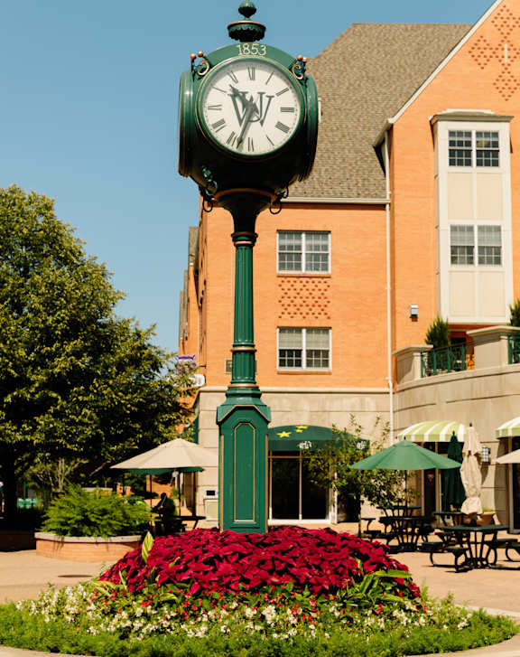 A green clock with roman numerals stands in front of a building.