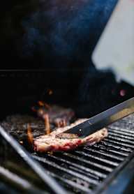 A steak is being grilled on a barbecue with visible flames and smoke.