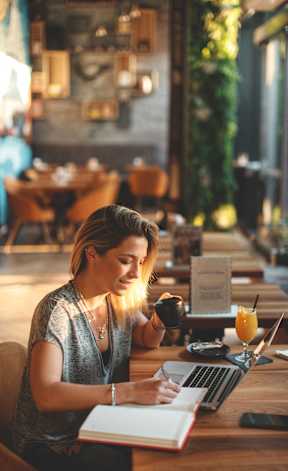a woman sitting at a table with her laptop and a cup of coffee