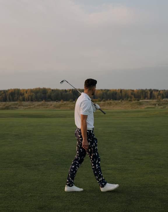 A man in a white shirt and patterned pants is holding a golf club.