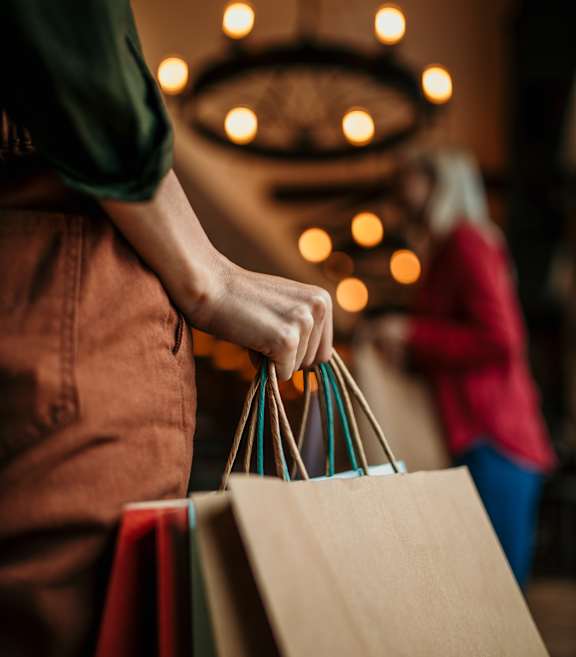 A person holding a brown paper bag with several other shopping bags in their hand.