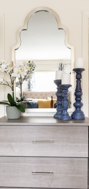 a mirror above a dresser with flowers and candles on it