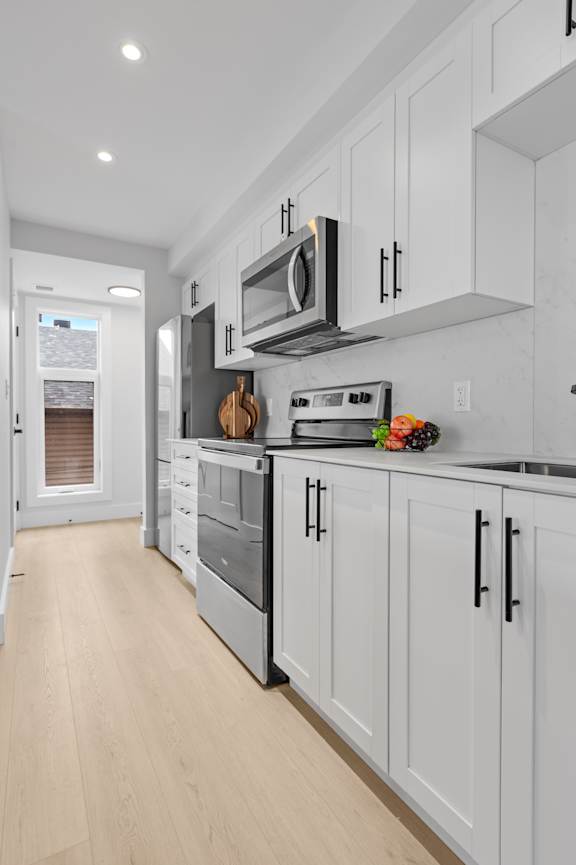 A white kitchen with a refrigerator, oven, and a white couch.