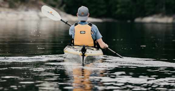 A man in a kayak paddles through a forest.