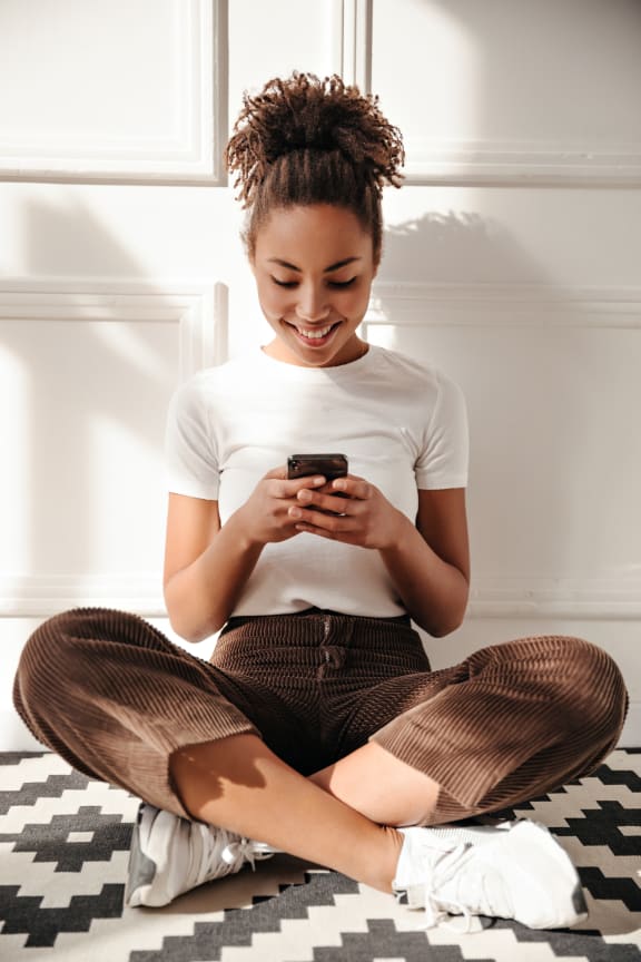 a woman sitting on the floor with her legs crossed and looking at her phone