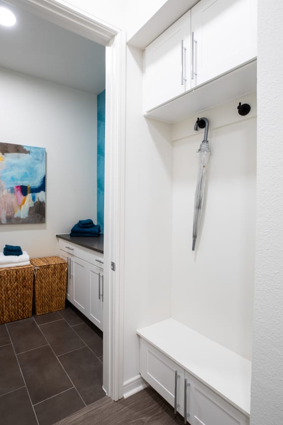 a walk in closet with white cabinets and a white bench with an umbrella on it
