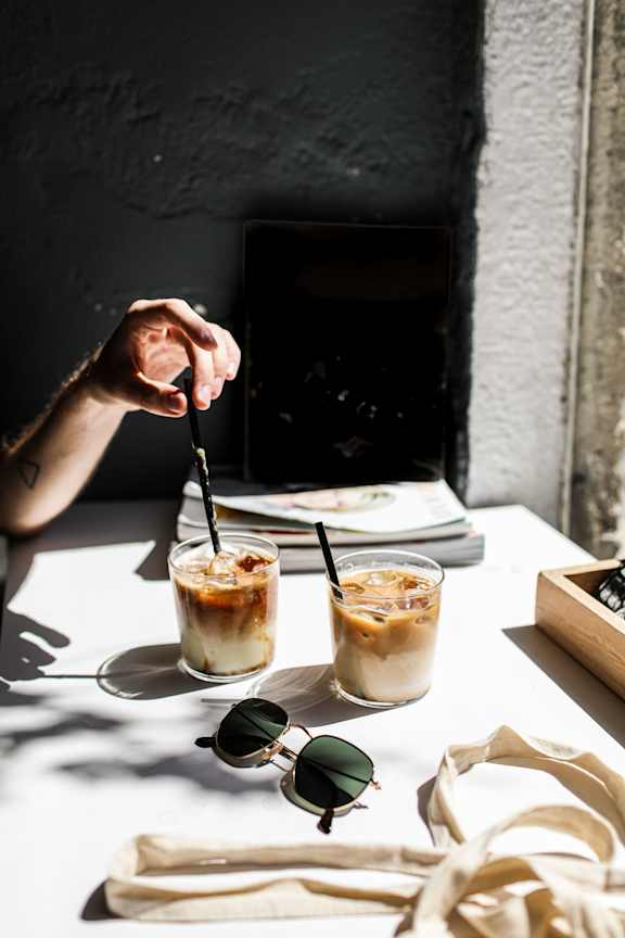 A person is holding a straw in their hand over a glass of iced coffee.