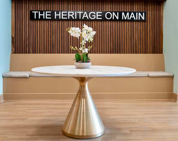 A white table with a gold pedestal stands in front of a wall with a sign that reads "The Heritage on Main.".