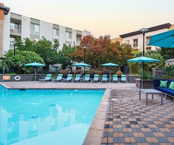 a swimming pool with blue chairs and umbrellas and a building in the background