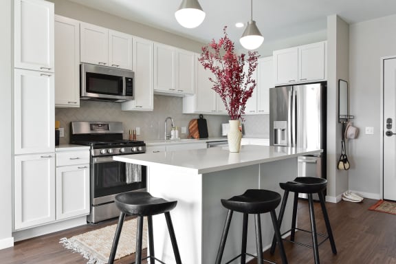 a kitchen with white cabinets and a white island with black stools