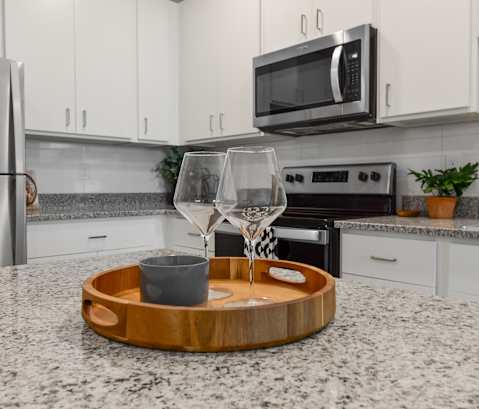 a kitchen with white cabinets and stainless steel appliances and a wooden tray with wine glasses