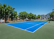 Thumbnail 1 of 7 - A blue tennis court surrounded by trees and buildings.