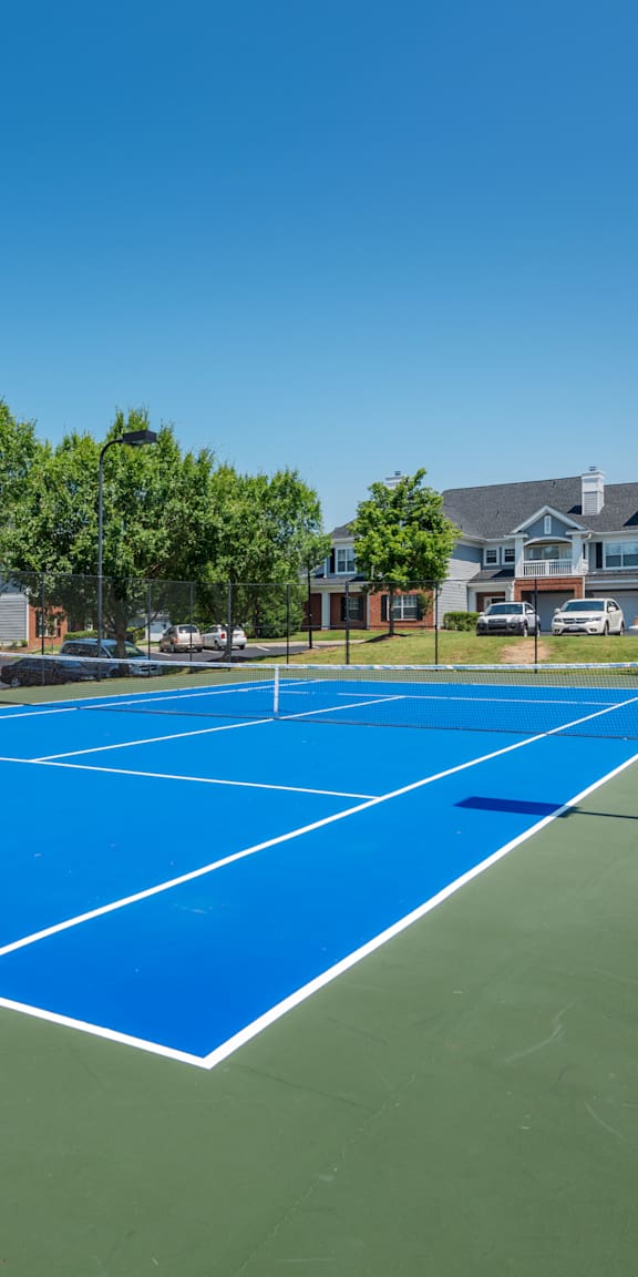 A blue tennis court surrounded by trees and buildings.