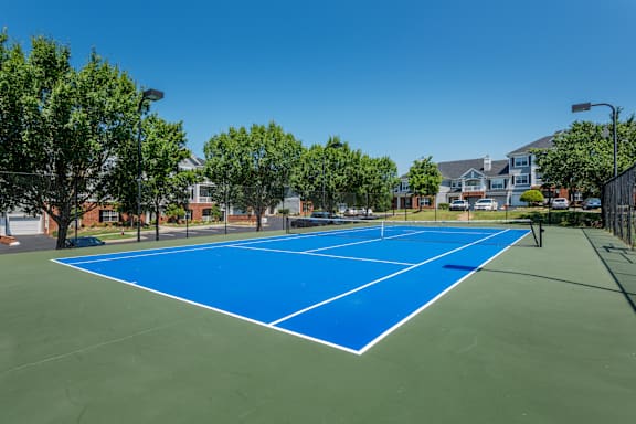 A blue tennis court surrounded by trees and buildings.