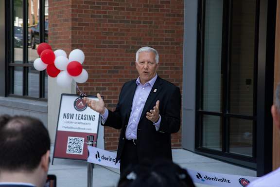 A man in a suit stands in front of a sign that says "Now Leasing" and "TheBulls.com".