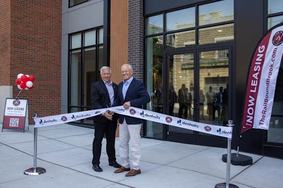 Two men are cutting a ribbon in front of a Denholz office.