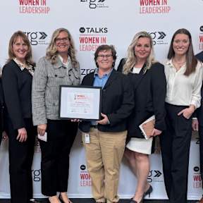 A group of women are standing in front of a banner for Women in Leadership.