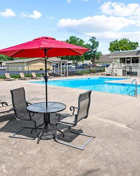 a table with a red umbrella and two chairs by a pool
