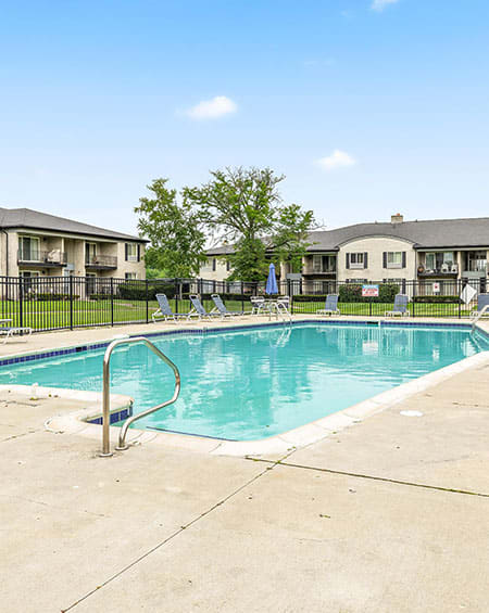 a swimming pool with a fence and apartment buildings in the background