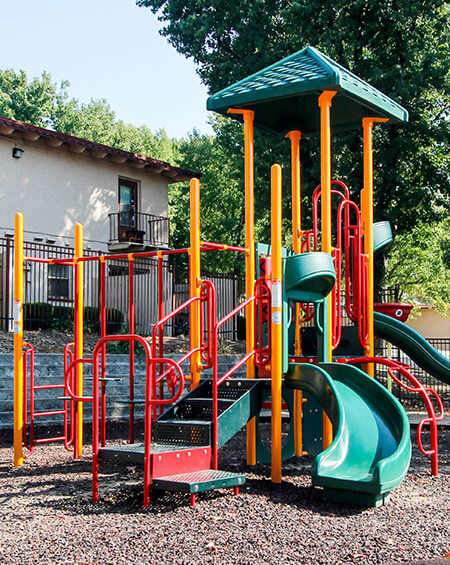 A playground with a green slide and red and yellow play equipment.