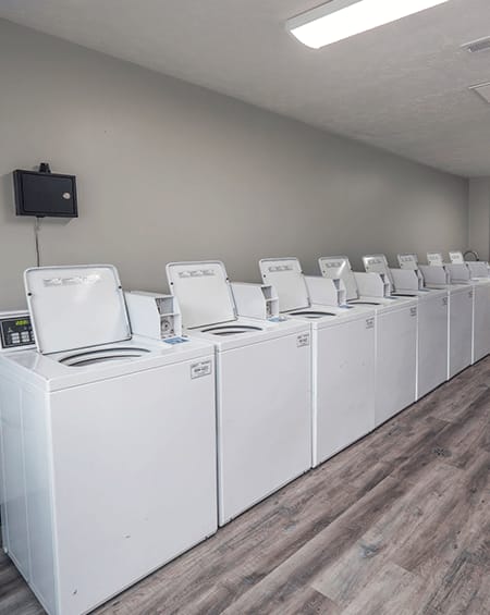 a row of white washers and dryers in a room with wood flooring