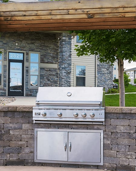 A silver built in BBQ grill with a cabinet underneath it.