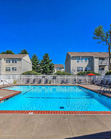 A swimming pool in front of a building with a white fence and trees.