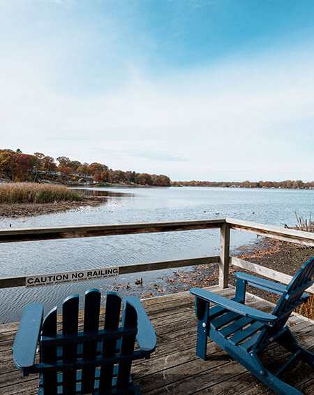Two blue chairs are on a wooden deck overlooking a body of water.