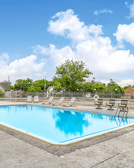 A swimming pool surrounded by chairs and trees.