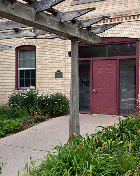 a red door on a brick building with a wooden pergola in front of it
