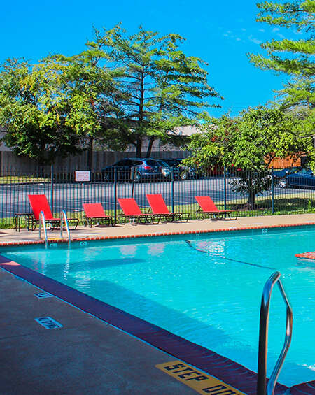 A pool with a step ladder and red chairs.