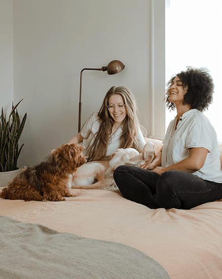 two women sitting on a bed with a dog