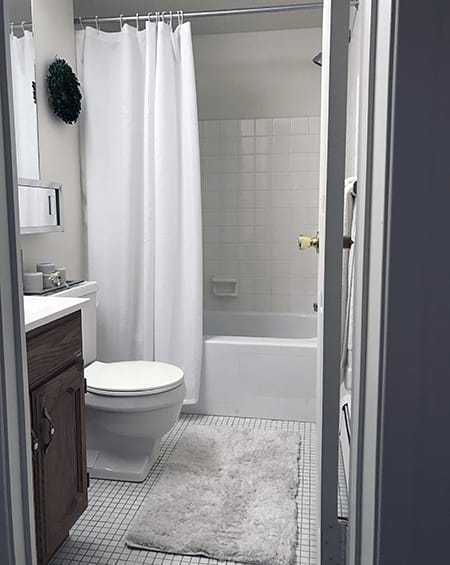 A white toilet sits in a bathroom next to a white shower curtain.