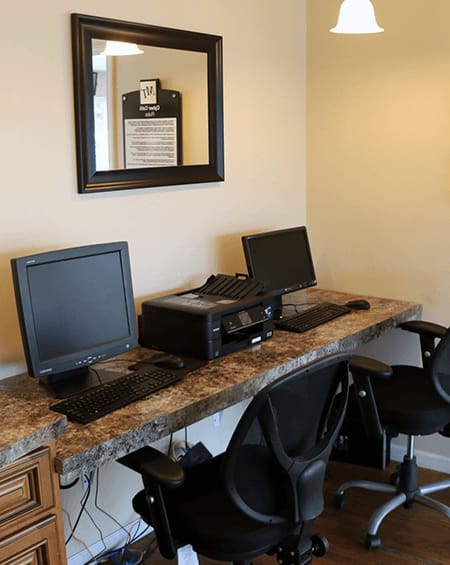 A black monitor and laptop on a granite desk with a black chair.