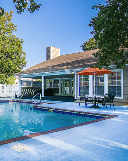 A pool in front of a house with a sun umbrella.